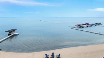 A beach with a dock, lounge chairs, and a fire pit.