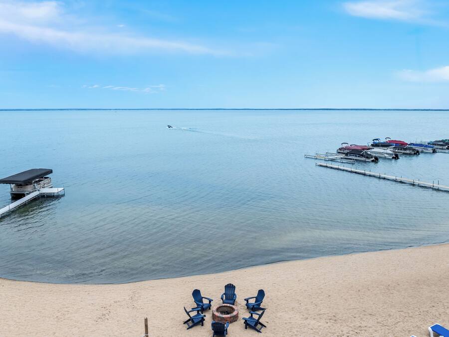 A beach with a dock, lounge chairs, and a fire pit.