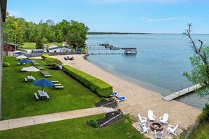 A lakeside property with a grassy lawn, outdoor seating, and a dock. - Beachfront Hotel (Houghton Lake)