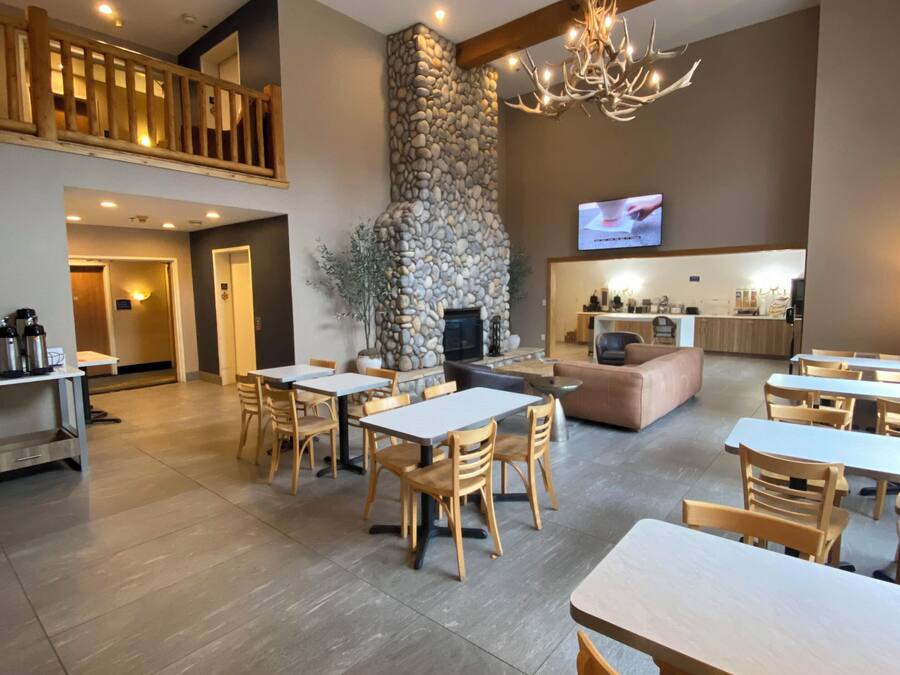 A spacious dining area with multiple tables and chairs, a stone fireplace, and a television mounted on the wall.
