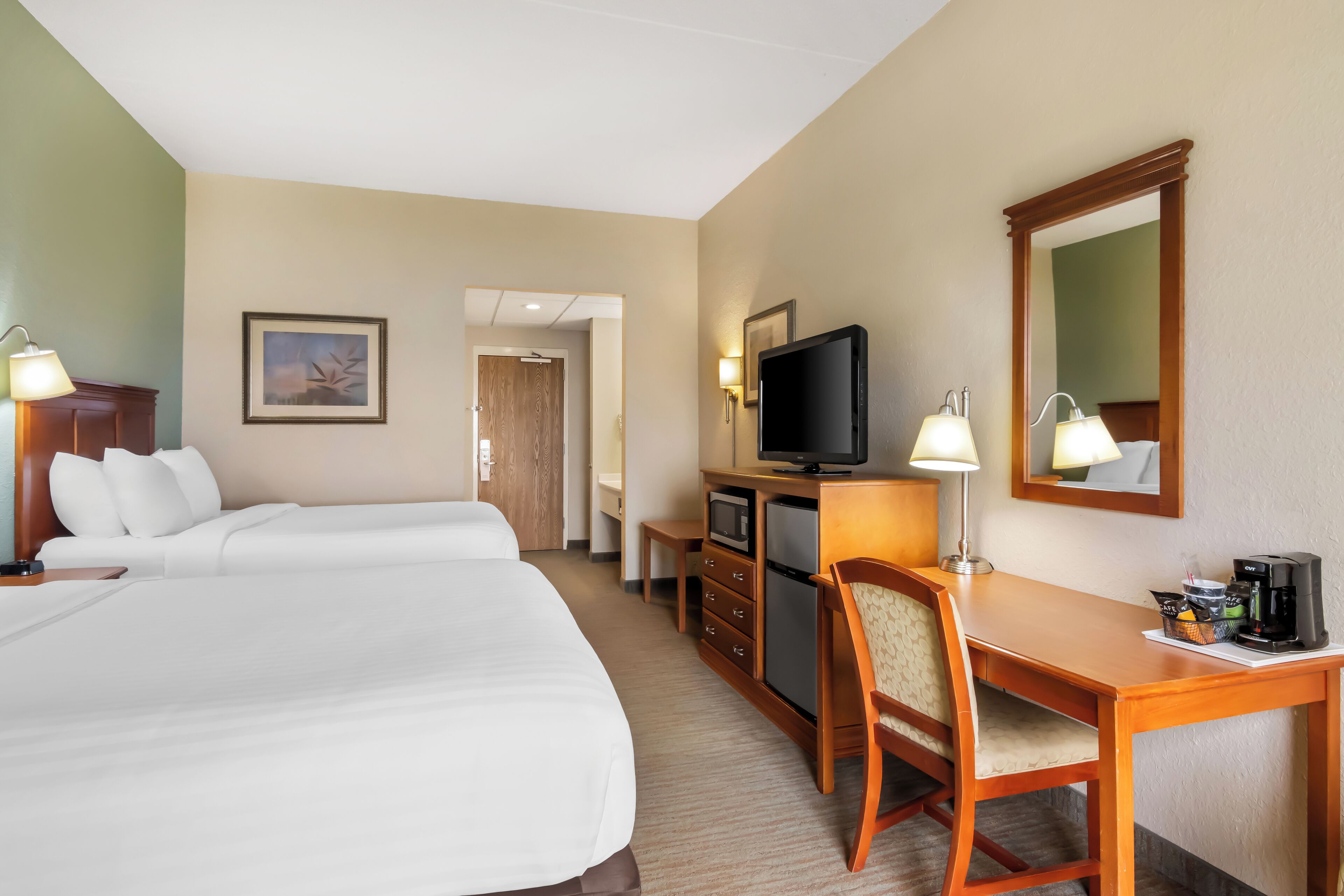 A hotel room with two beds, a desk with a chair, a television, a coffee maker, and a mirror.