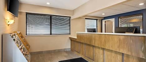 Een hotel receptie met een houten balie, een flatscreen televisie aan de muur en een trap met een zwart tapijt.