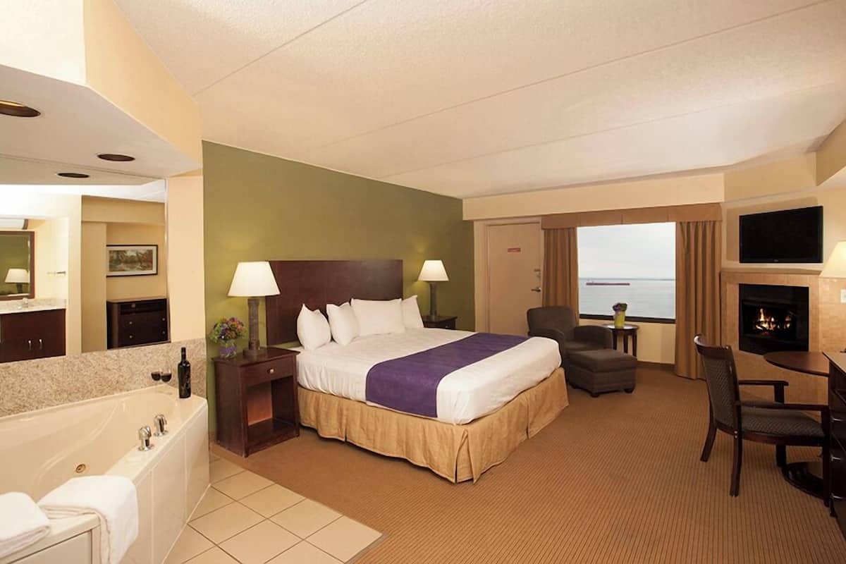 Une chambre d’hôtel avec un lit, un bureau, une chaise, une cheminée, une télévision et une vue sur la mer.