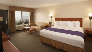 Ein Hotelzimmer mit einem großen Bett, einem Schreibtisch, einem Stuhl, einem kleinen Tisch und Meerblick aus dem Fenster.