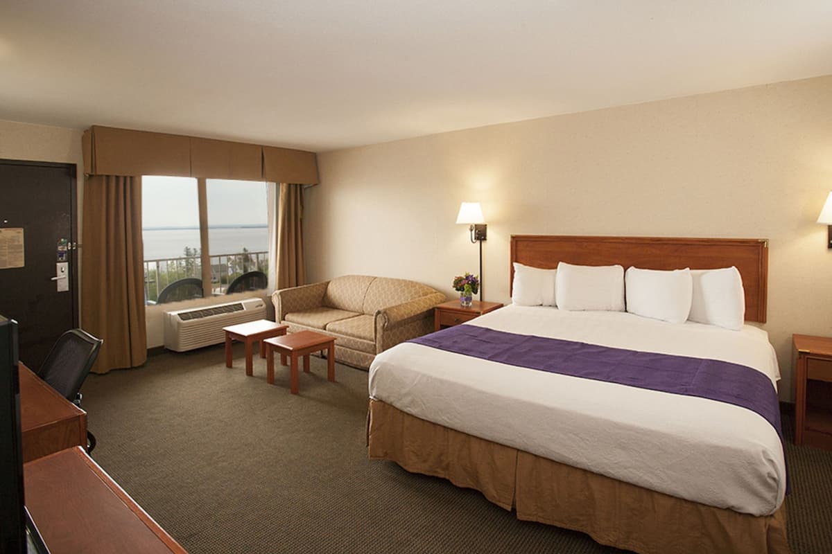 Une chambre d’hôtel avec un grand lit, un bureau, une chaise, une petite table et une vue sur la mer par la fenêtre.