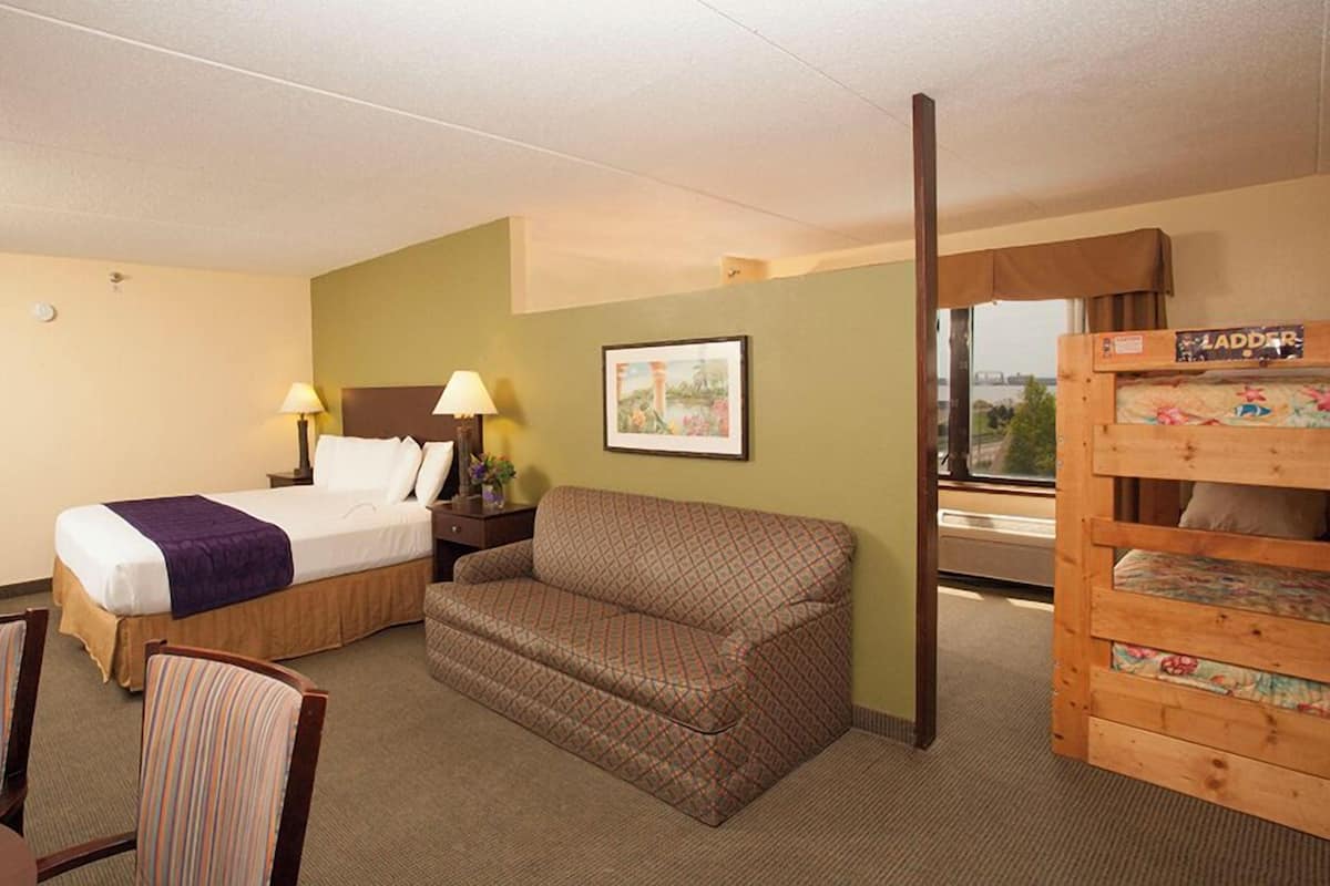 Une chambre d’hôtel avec un lit, un canapé, un bureau avec une lampe, une chaise et une vue sur l’extérieur.