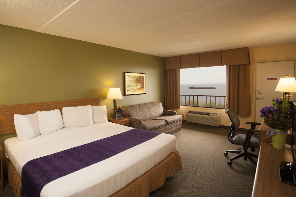 Une chambre d’hôtel avec un grand lit, un bureau, une chaise, un canapé et une vue sur la mer.