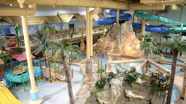 Ein großer Indoor-Wasserpark mit Rutschen, einer Kletterwand und einem Schwimmbecken.