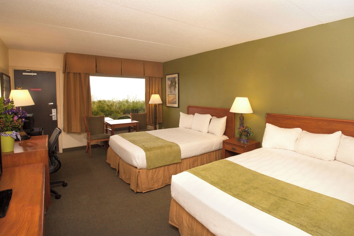 Une chambre d’hôtel avec deux lits, un bureau, des chaises, des lampes et une fenêtre donnant sur un paysage agréable.