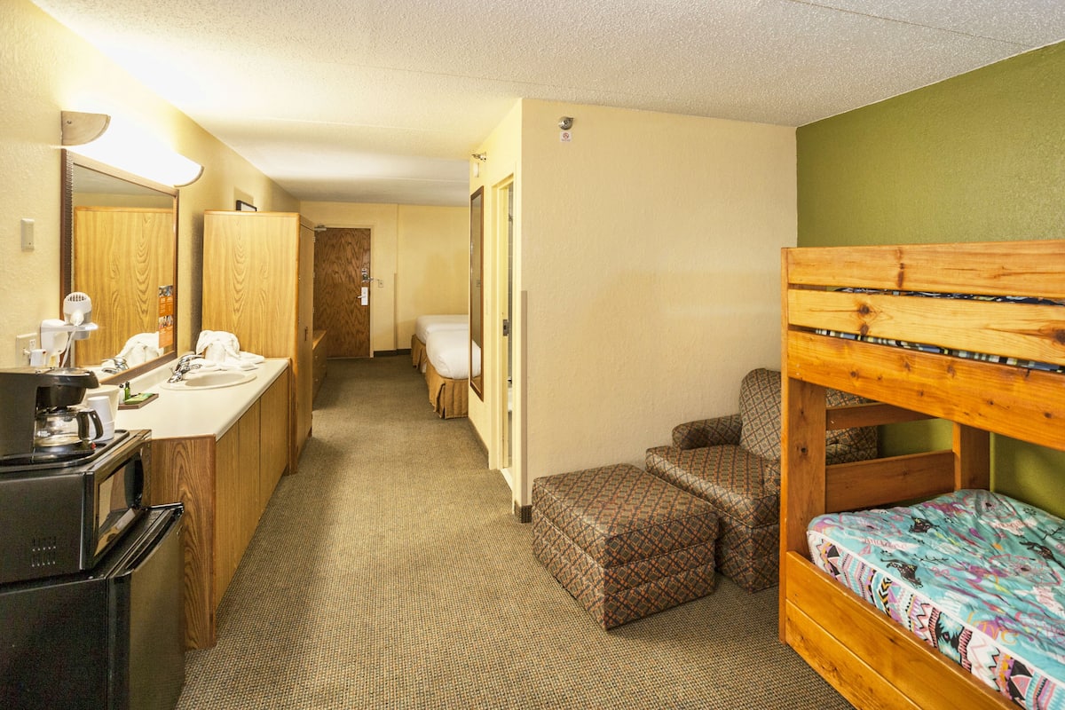 Une chambre d’hôtel avec un lit superposé, une kitchenette, une salle de bain avec un miroir et un petit coin salon.