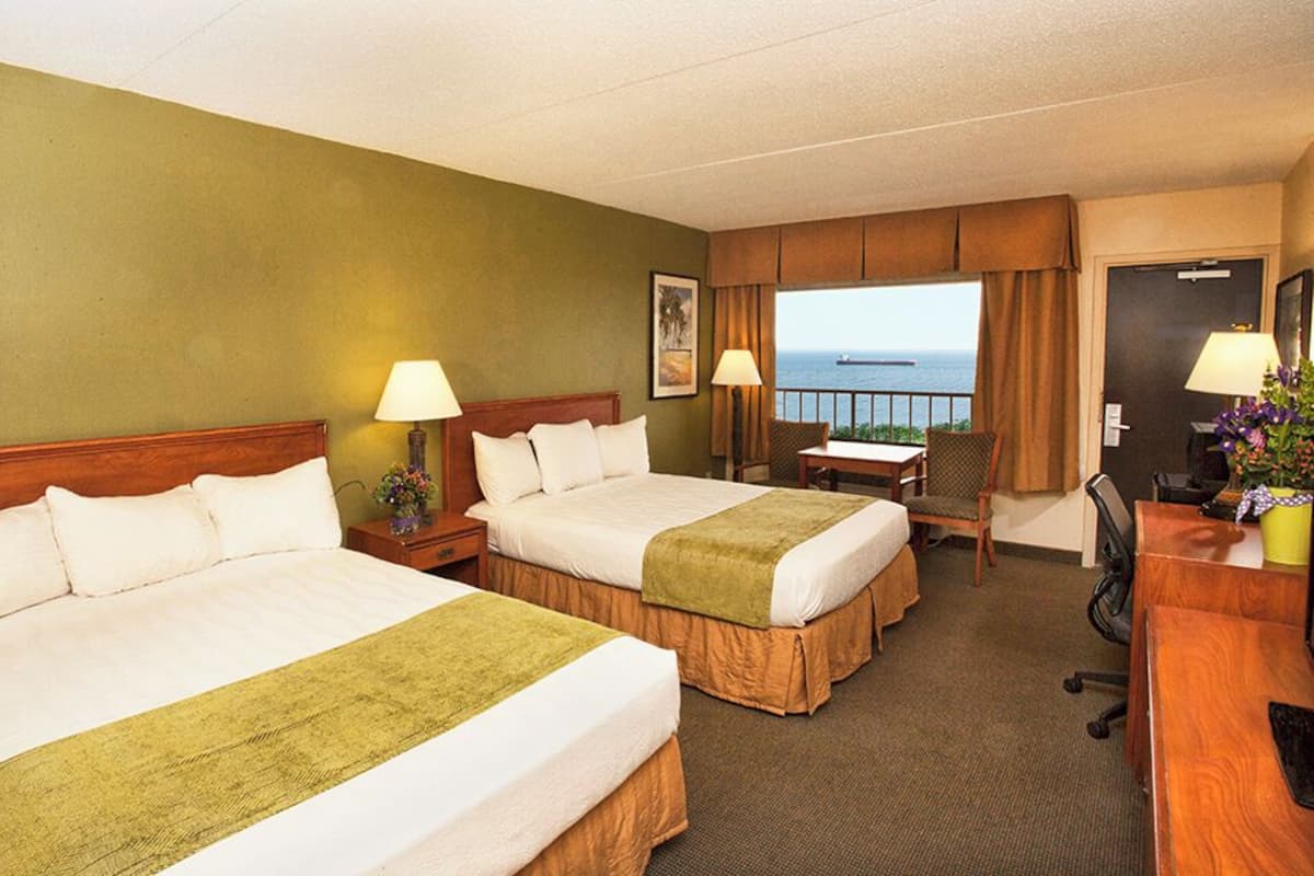 Une chambre d’hôtel avec deux lits, un bureau, une chaise, une lampe et une vue sur l’océan.