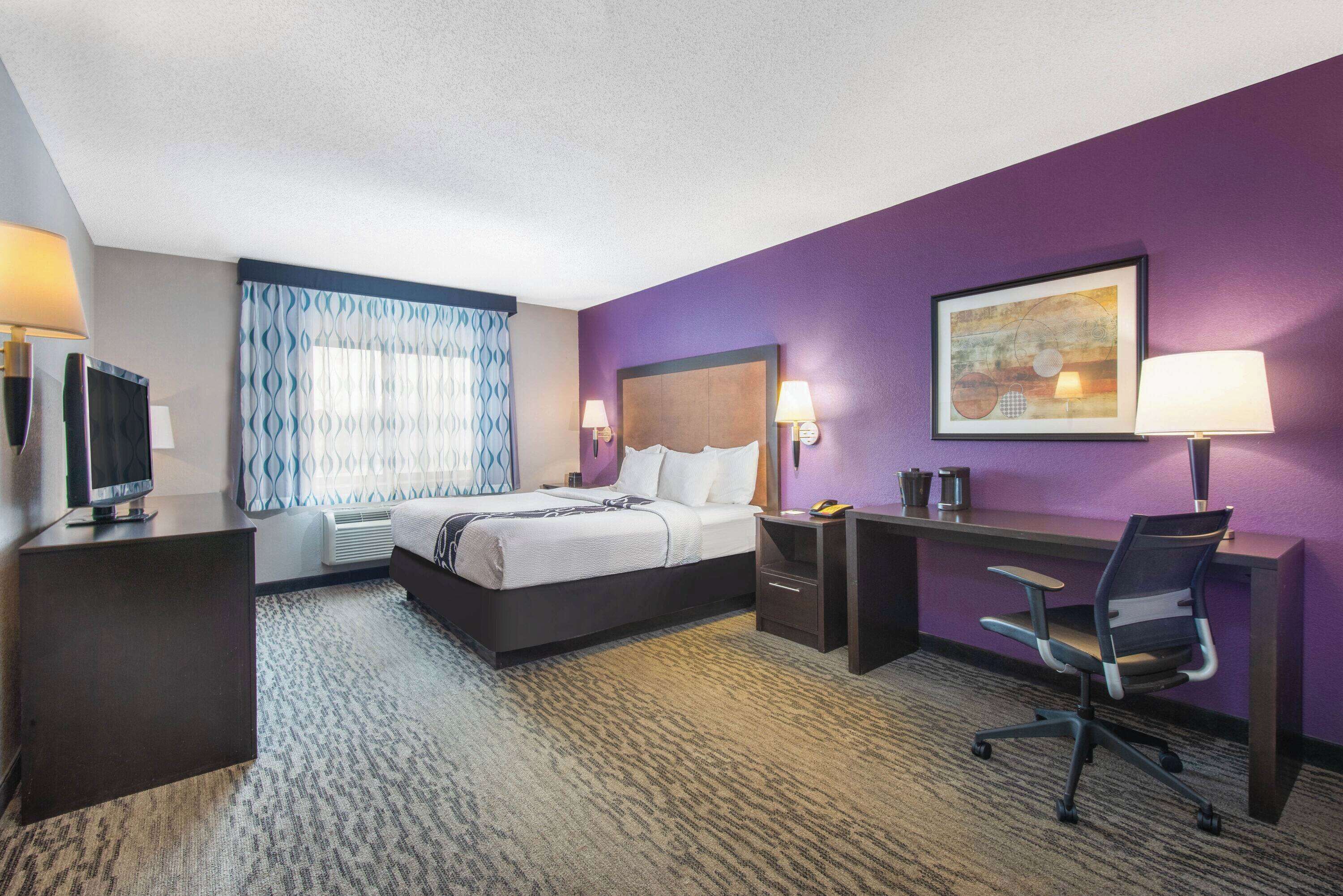 A hotel room with a bed, desk, chair, and a television.