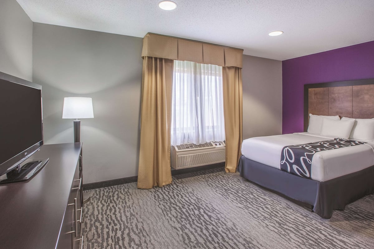 A hotel room with a bed, a desk with a lamp, and a window with curtains.