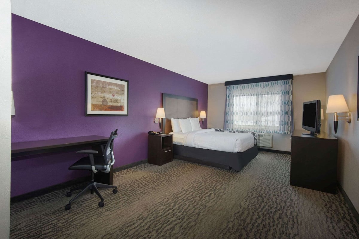 A hotel room with a bed, desk, chair, bedside lamps, and a television.