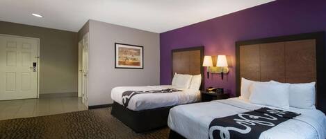 A hotel room with two beds, a purple accent wall, and a door to the left.