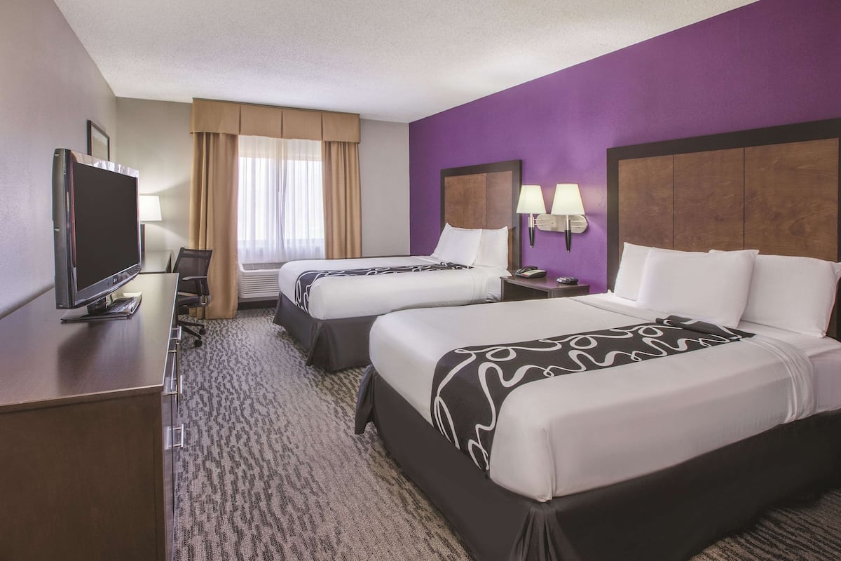 A hotel room with two beds, a desk with a TV, and a window with curtains.