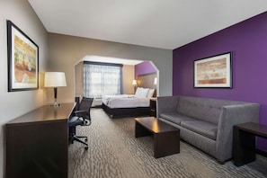 A hotel room with a bed, a sofa, a desk, and two chairs.