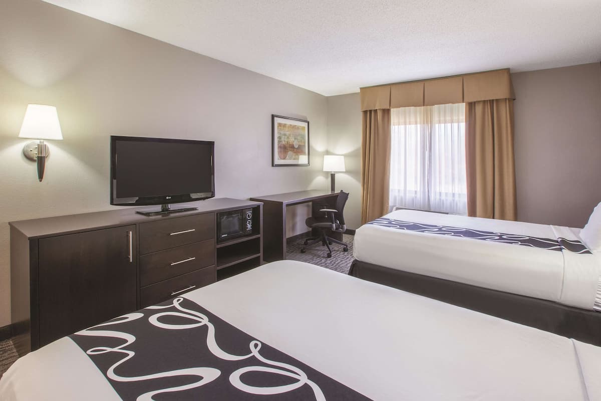 A hotel room with two beds, a desk, a television, and a lamp.
