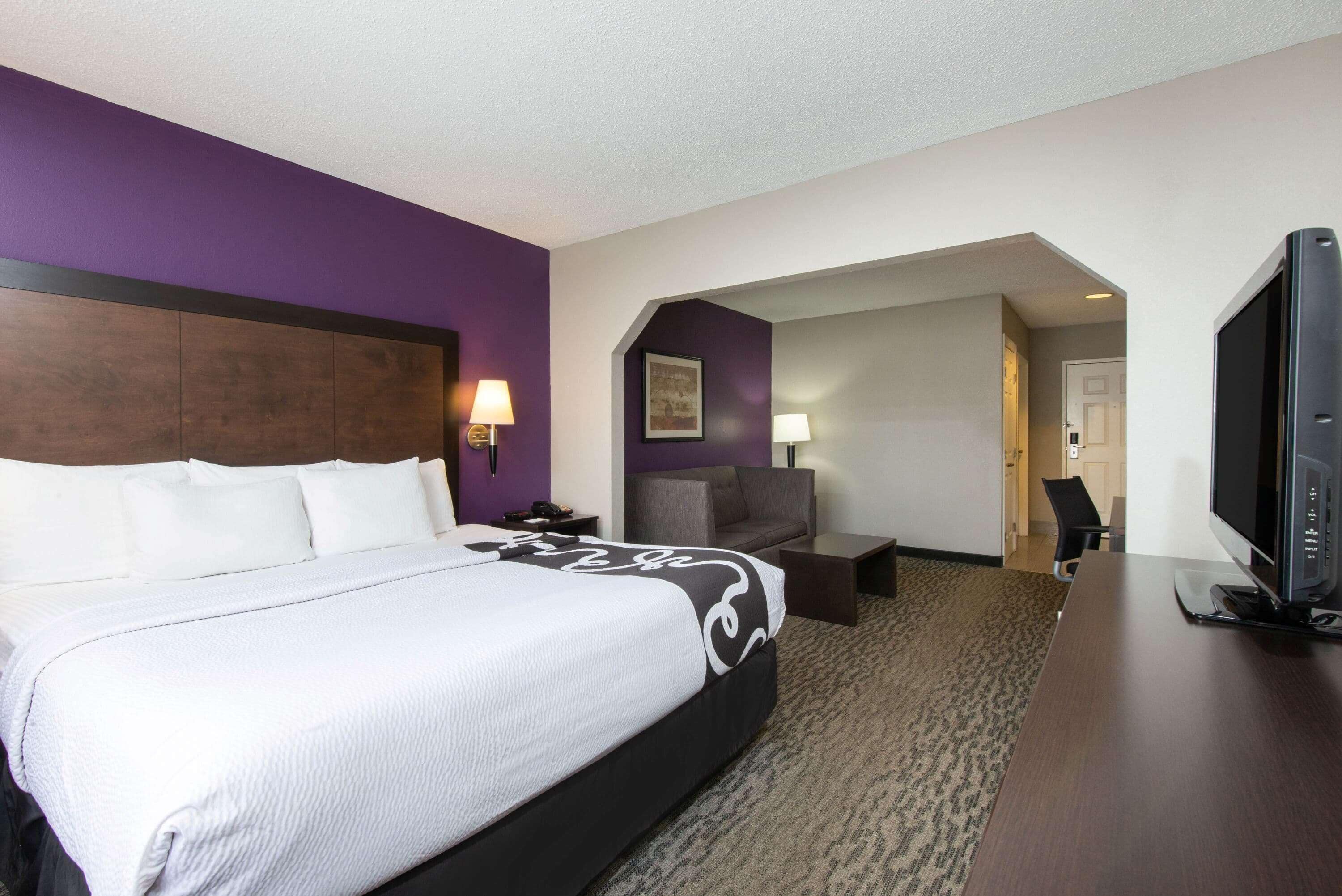 A hotel room with a large bed, a desk, a television, and a sofa.