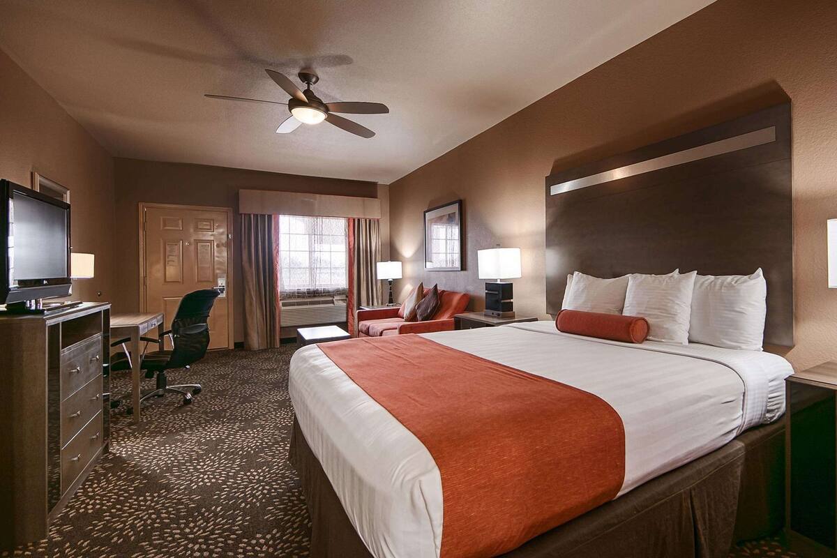 Habitación de hotel con cama, escritorio, silla y ventilador de techo.