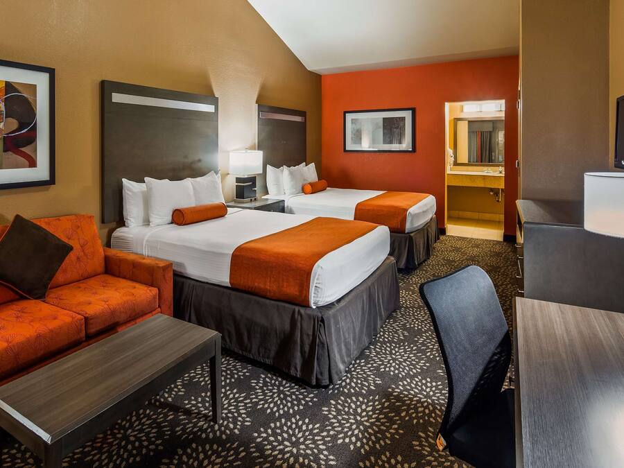 A hotel room with two beds, a sofa, a desk, and a TV.