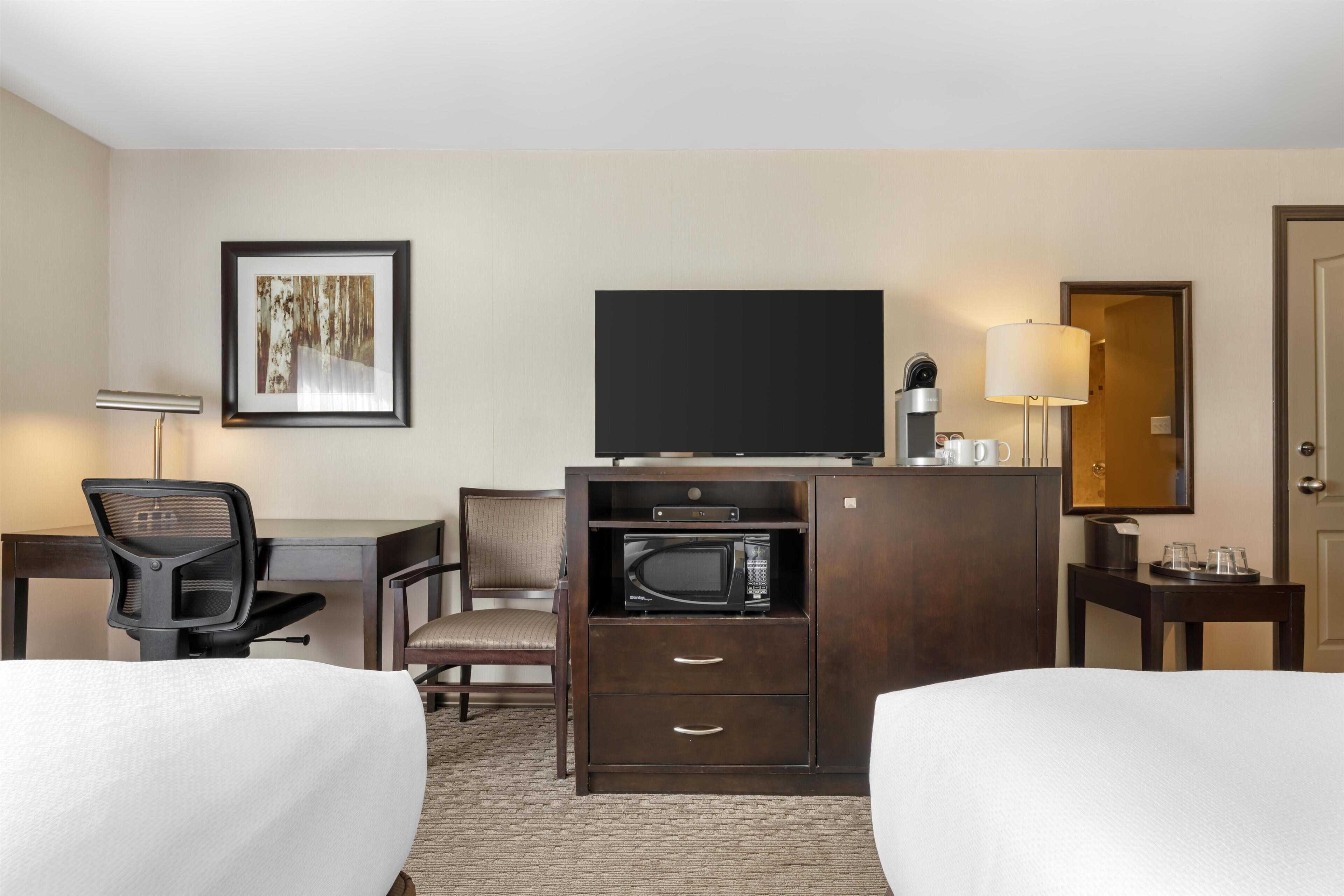 A hotel room with a bed, a desk, a chair, a television, a microwave, and a framed picture on the wall.