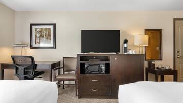 A hotel room with a bed, a desk, a chair, a television, a microwave, and a framed picture on the wall.