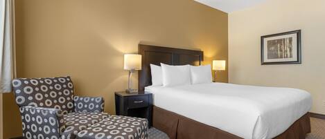 A hotel room with a large bed, a chair, a nightstand, and a lamp.