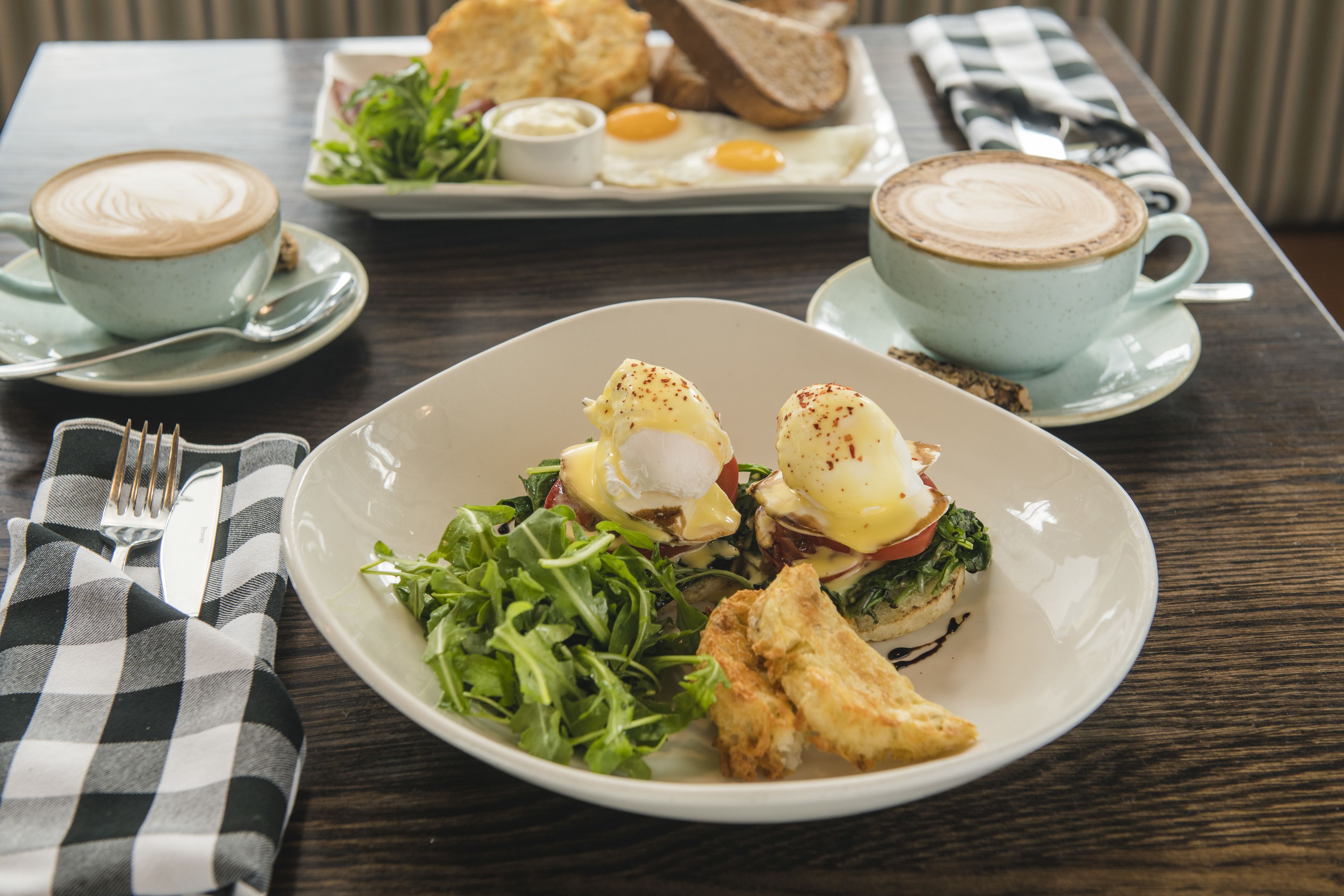 Desayuno con huevos benedictinos, una taza de café y una ensalada sobre una mesa de madera.