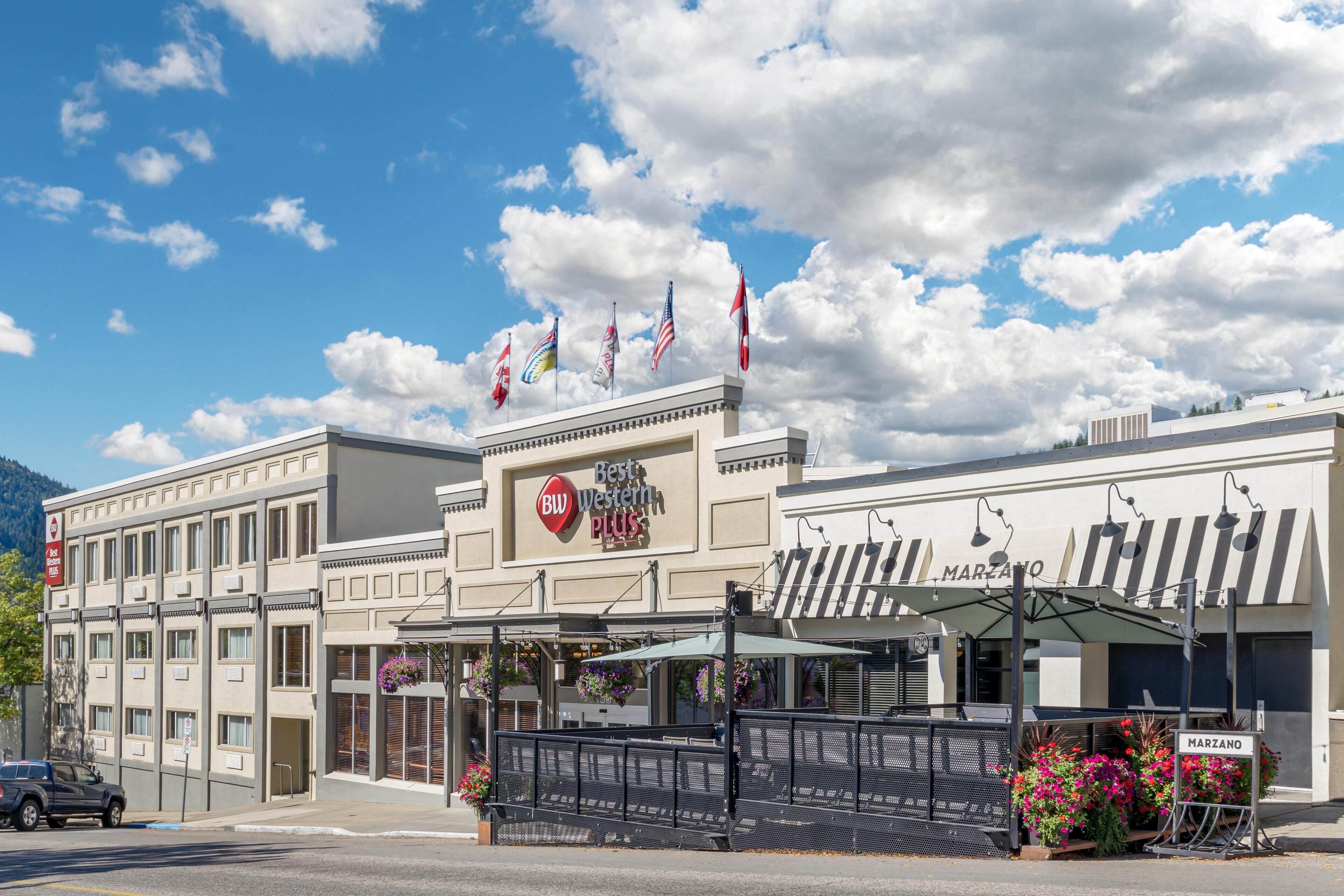 A hotel with a 'Best Western Plus' sign, outdoor seating with umbrellas, and multiple flags.