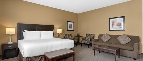 Habitación de hotel con una cama grande, un sofá, dos sillones, una mesita y un banco.