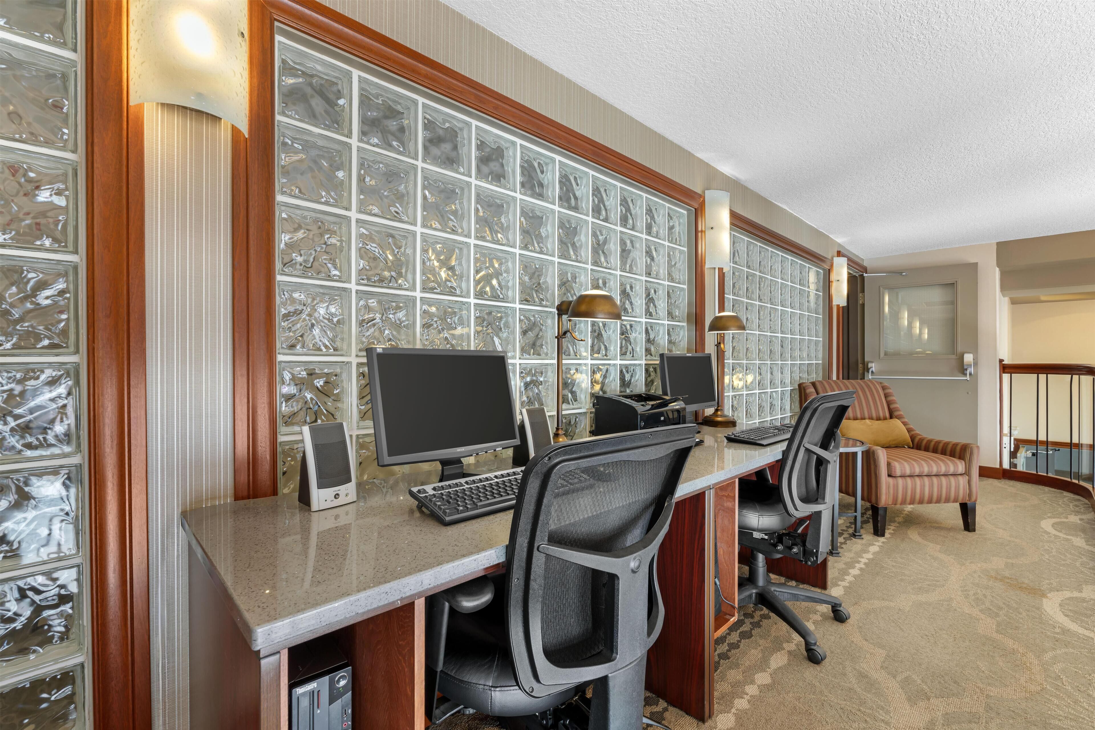 Ein Hotelzimmer mit einem langen Schreibtisch, zwei Monitoren, einer Tastatur und zwei Bürostühlen.