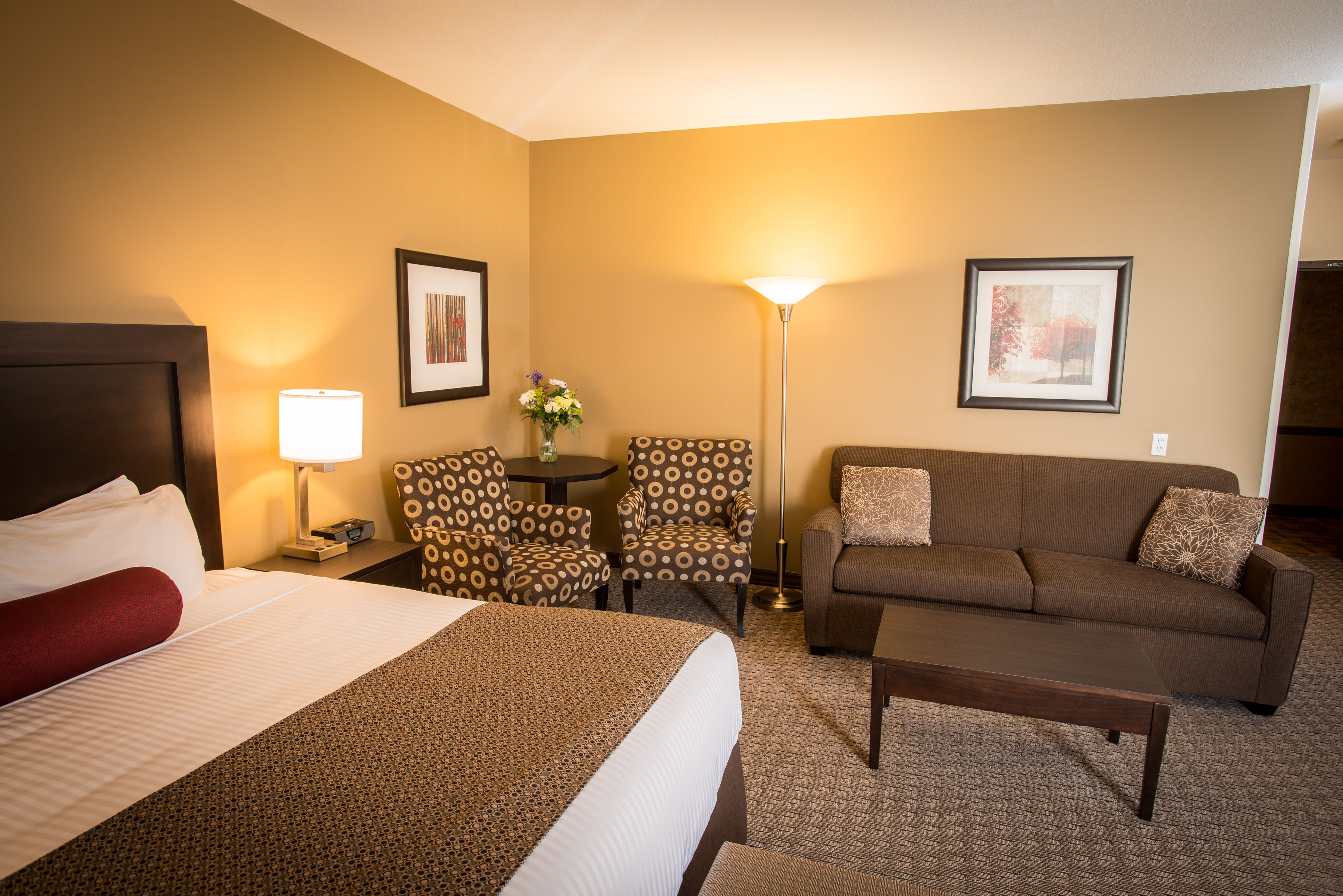 A hotel room with a bed, a sofa, a coffee table, a lamp, and two chairs.
