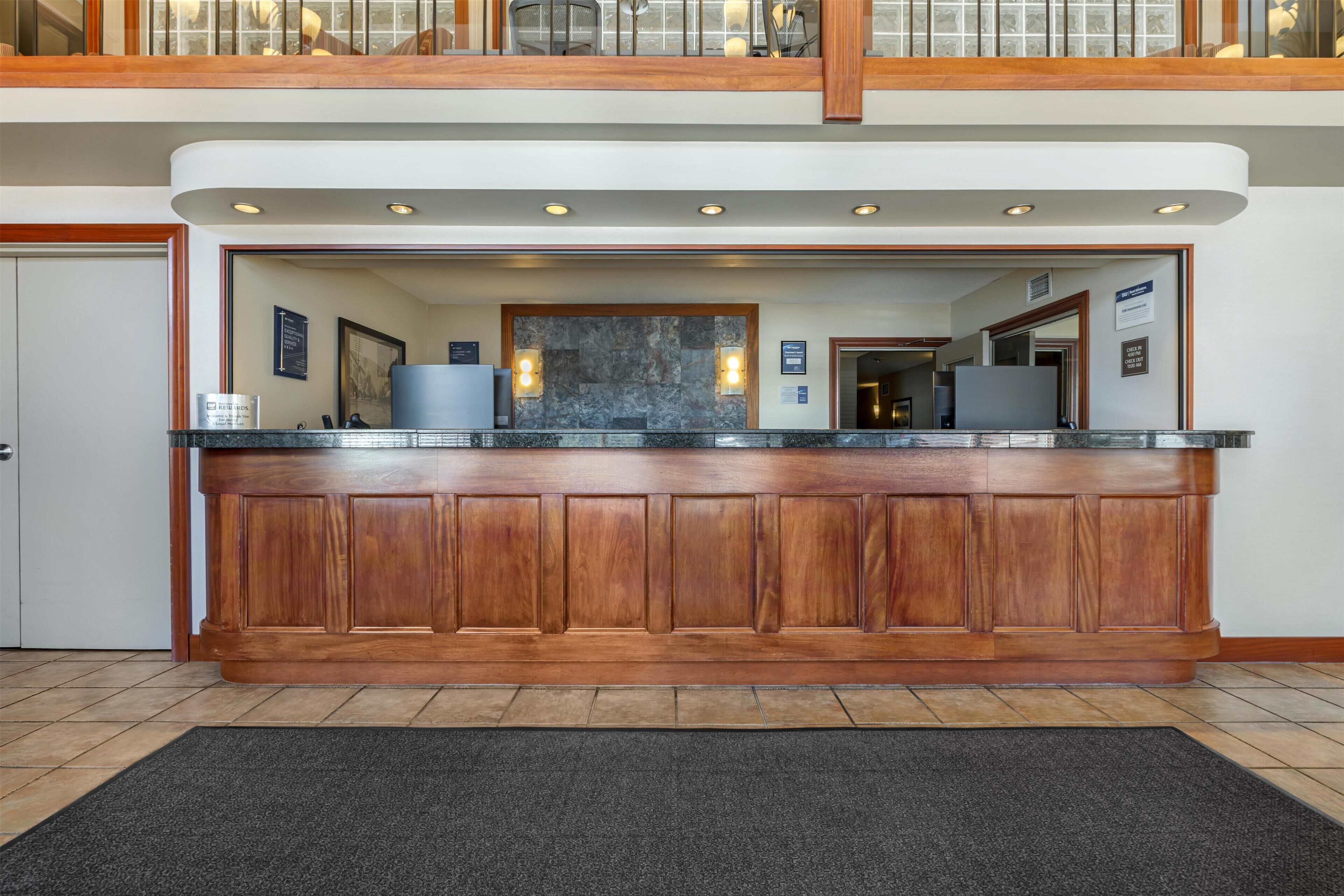 Zona de recepción con mostrador de madera, pared de mármol y alfombra negra.