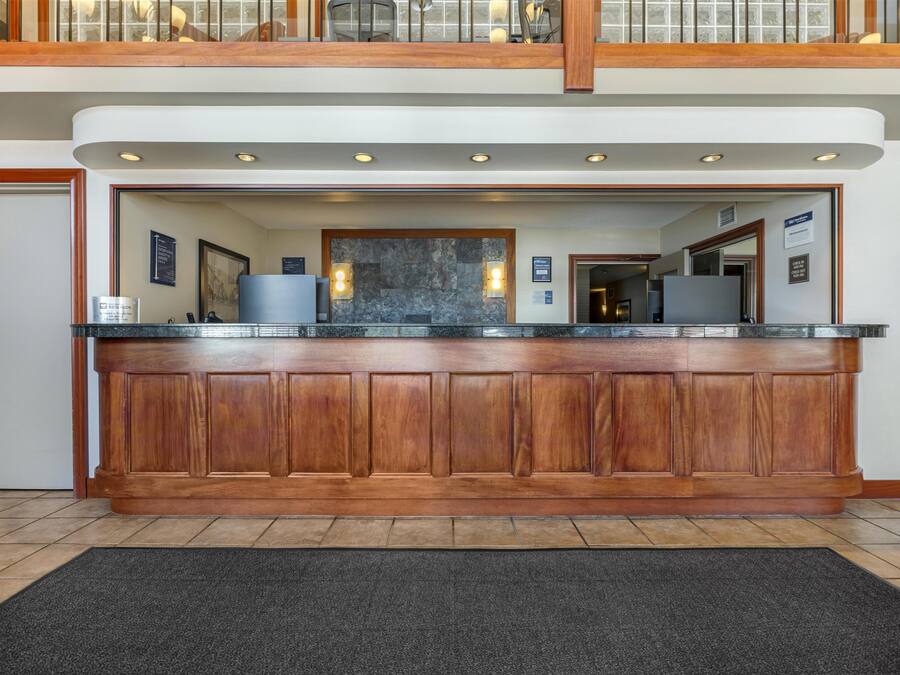 Zona de recepción con mostrador de madera, pared de mármol y alfombra negra.