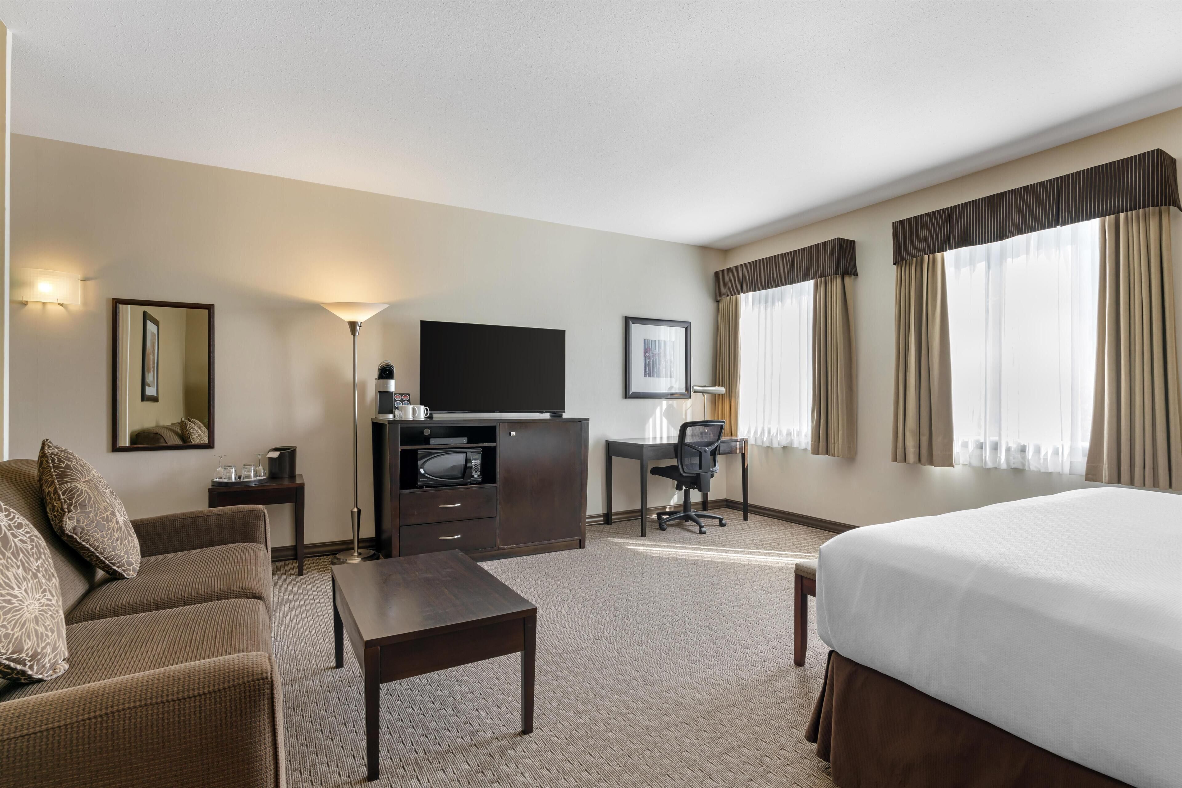 A hotel room with a bed, a desk, a chair, a television, and a sofa.