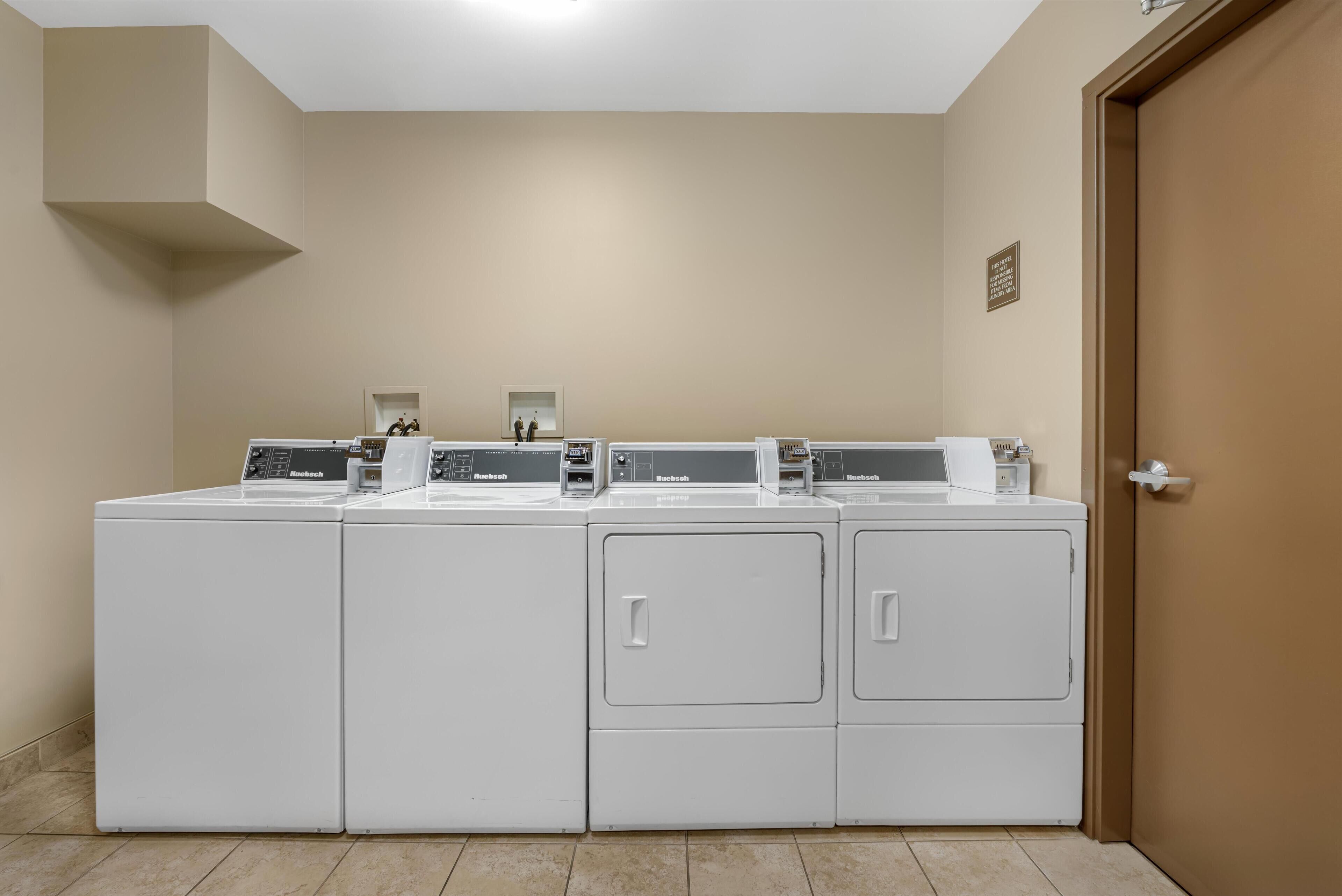 A laundry room with four white front-loading washing machines and dryers, a small window, and a door with a handle.