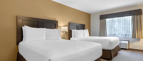 A hotel room with two beds, a window with curtains, a lamp, and a carpeted floor.