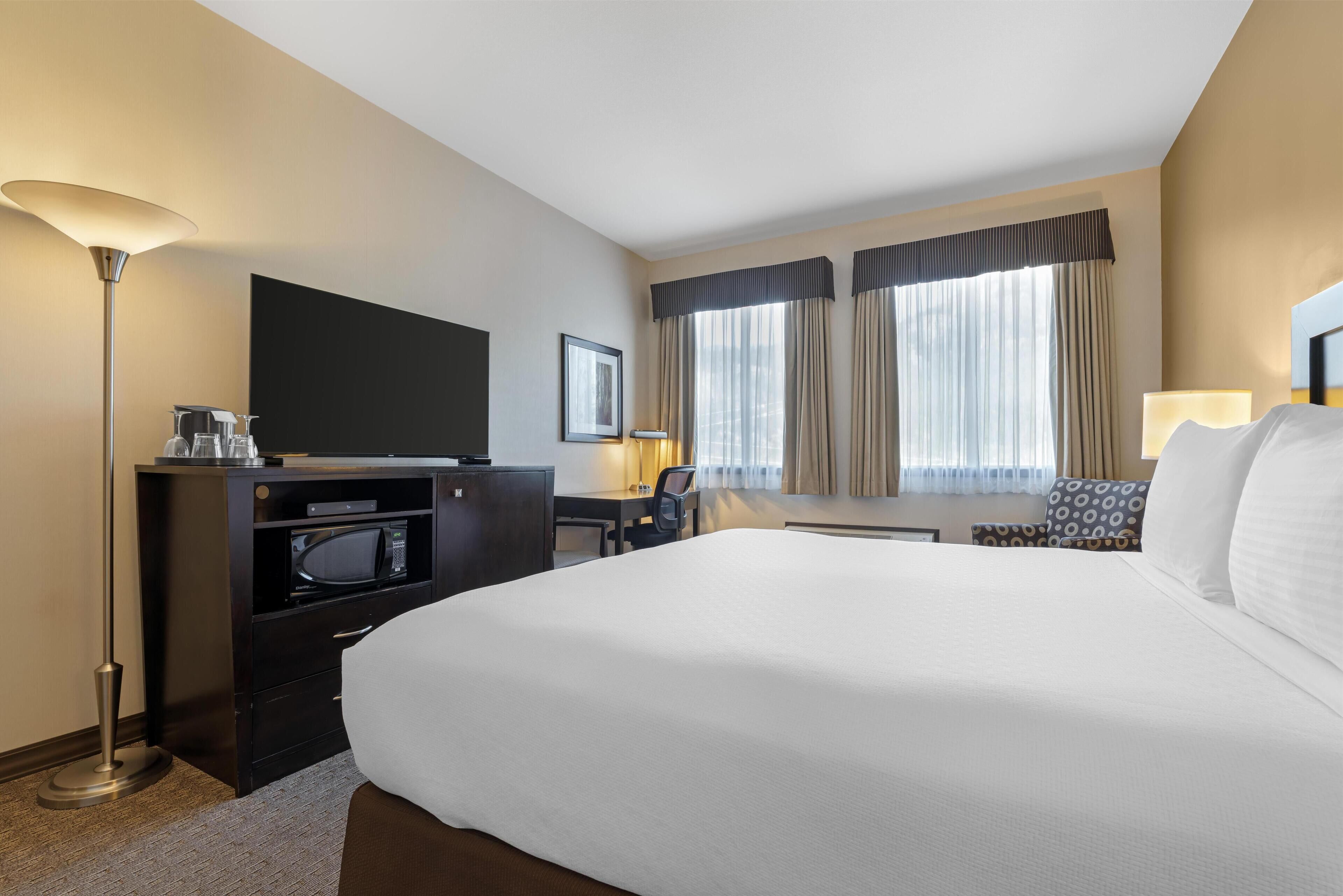 Habitación de hotel con una cama grande, un escritorio con televisor de pantalla plana, microondas, lámpara y ventana con cortinas.