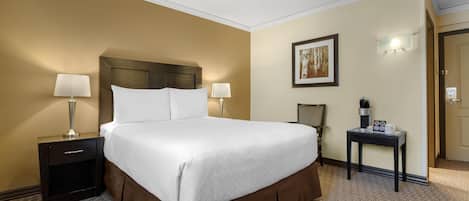 Habitación de hotel con una cama grande, dos mesitas de noche con lámparas, una cafetera y un cuadro enmarcado en la pared.