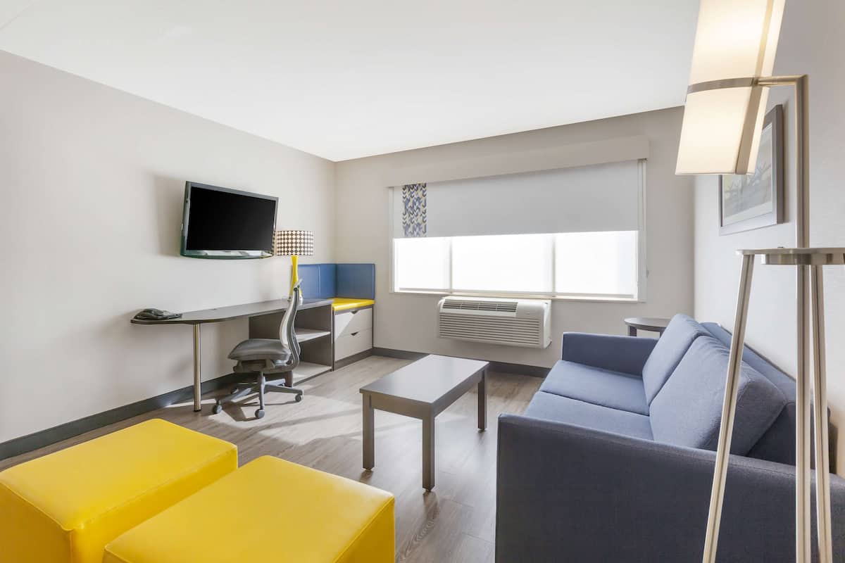Una habitación de hotel moderna con una televisión de pantalla plana, un escritorio con una silla, un sofá y una mesa de centro.