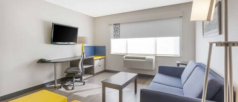 A modern hotel room with a flat-screen TV, a desk with a chair, a sofa, and a coffee table.