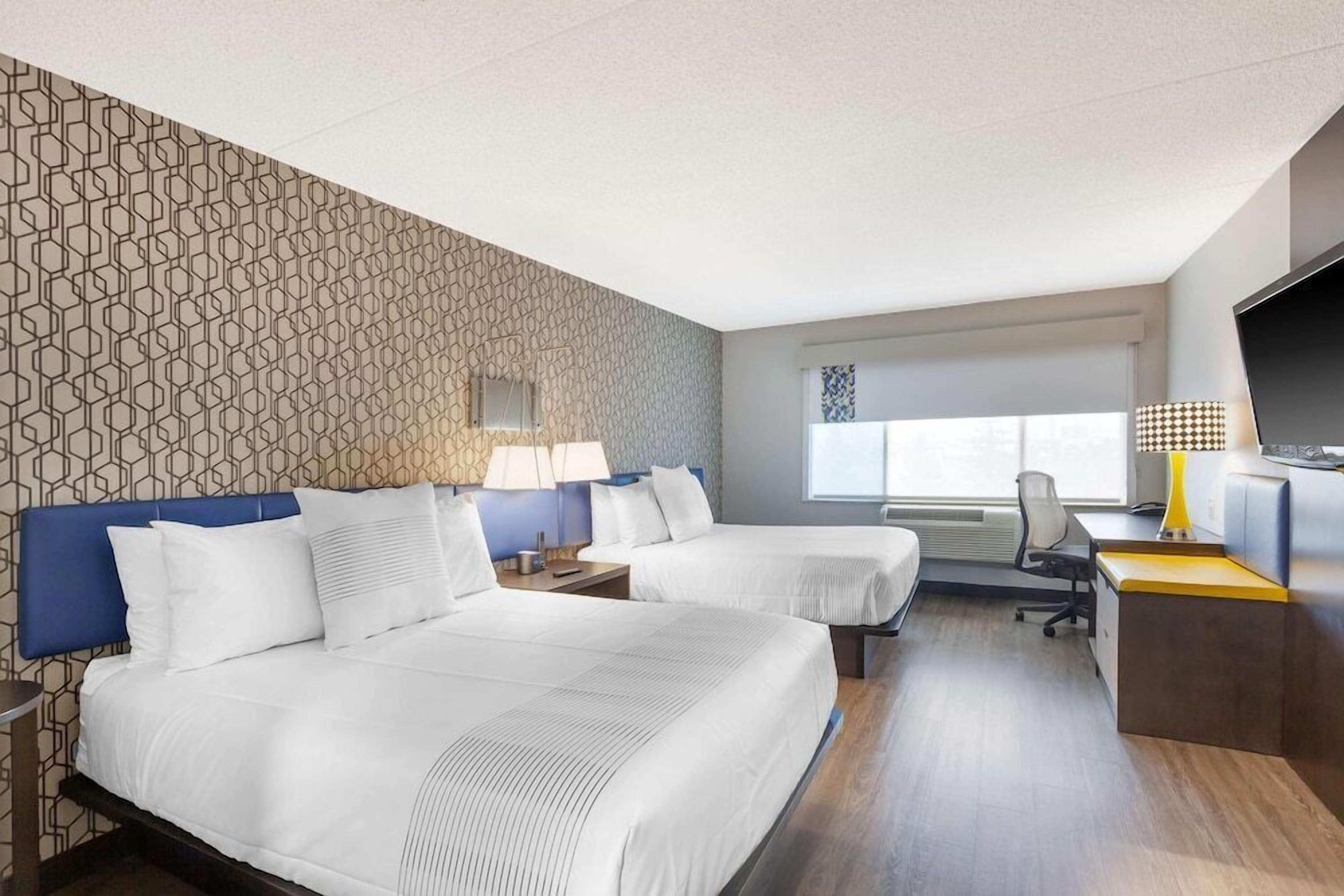 A hotel room with two beds, a desk, a chair, a TV, and a window.
