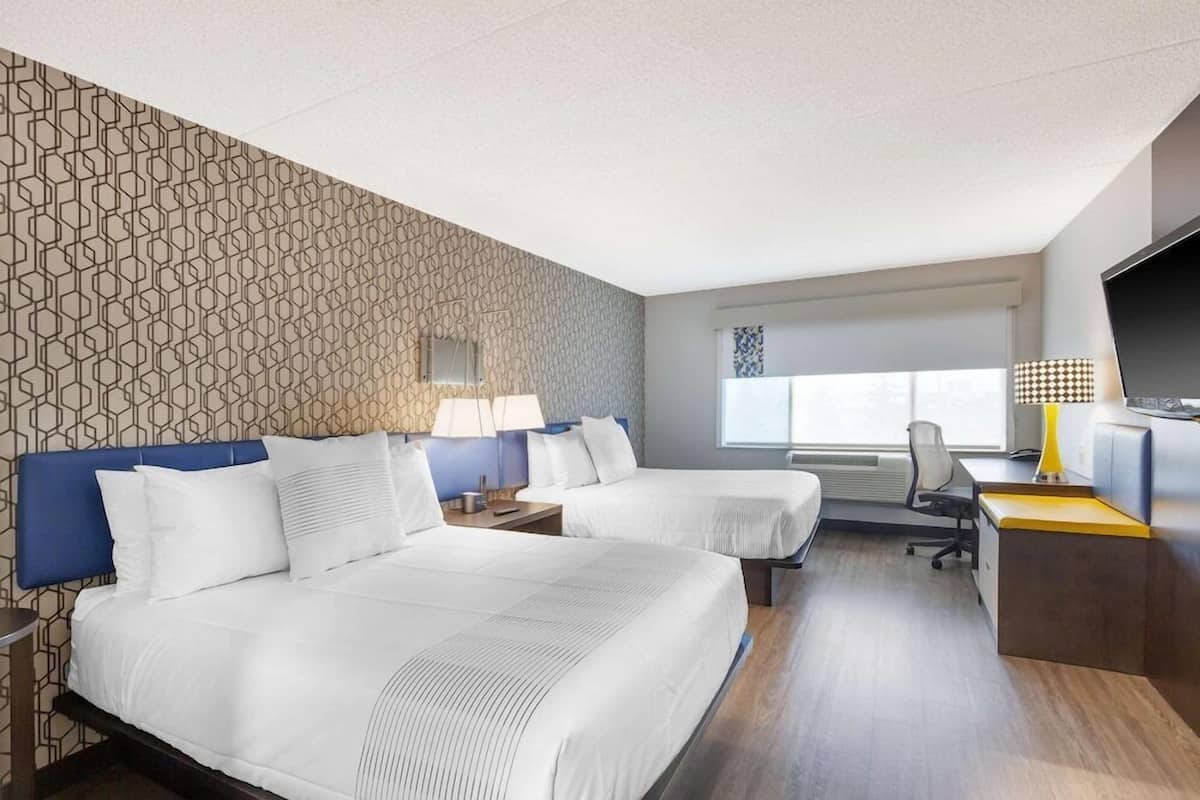 Habitación de hotel con dos camas, un escritorio, una silla, un televisor y una ventana.