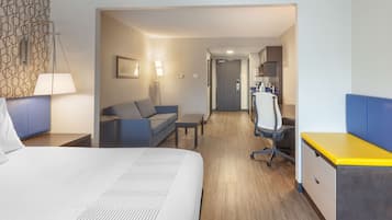 A hotel room with a bed, a desk, a chair, a sofa, and a kitchenette area.