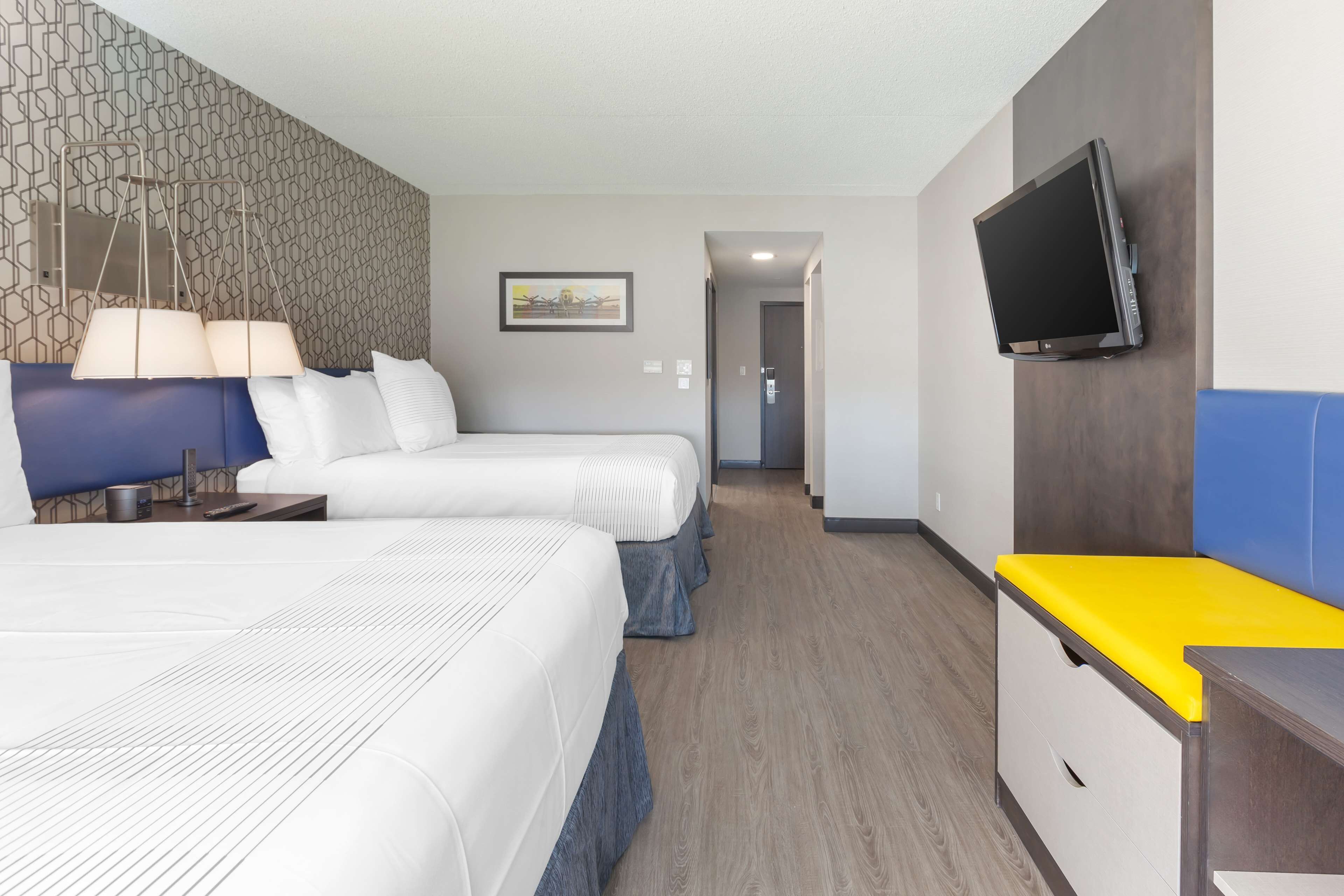 A hotel room with two beds, a TV mounted on the wall, and a desk with a yellow surface.
