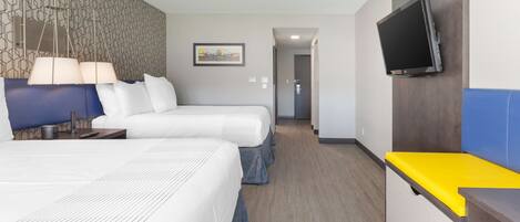 A hotel room with two beds, a TV mounted on the wall, and a desk with a yellow surface.