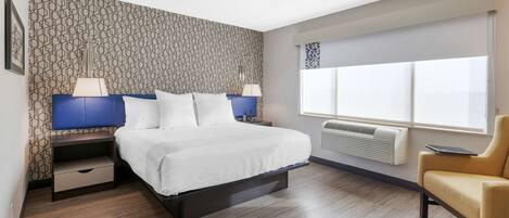 A modern hotel room with a bed, bedside tables, a chair, and a large window.