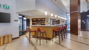 Zona de bar moderna con barra, taburetes y un refrigerador lleno de bebidas.