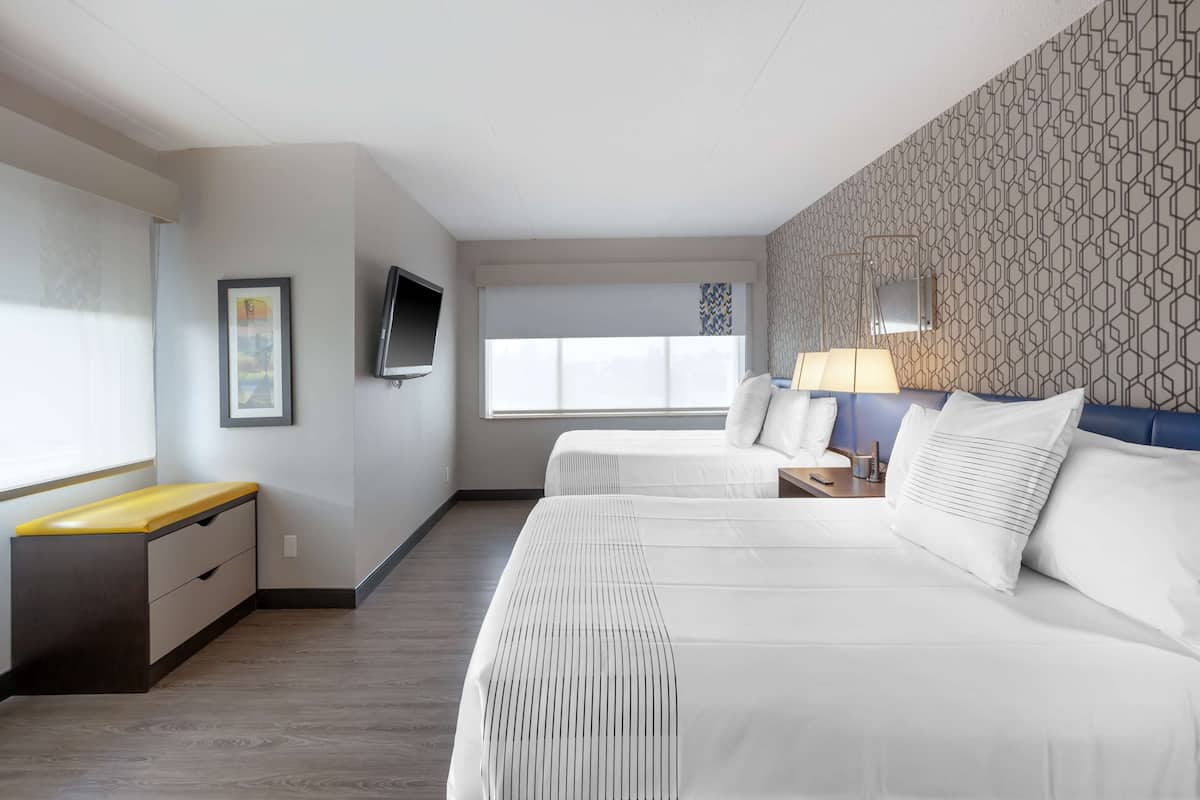 Habitación de hotel con dos camas, un escritorio, un televisor y una ventana con persianas.